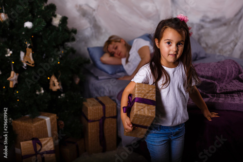 little girl opens gifts while mother is sleeping