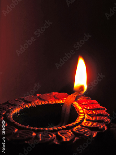 Close up isolated low key diwali oil clay lamp,chirag or panti on a dark orange black background with bright orange red light illuminating clay lamp