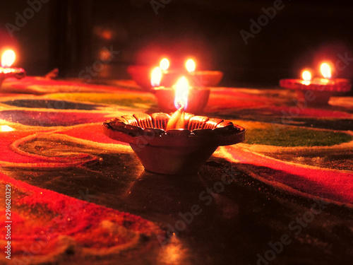 low angle shot of diwali oil clay lamps with intricate red green coloured design placed on multicoloured green blue red rangoli