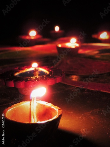low angle view of diwali oil clay lamps with intricate red green colored design placed in a row and diagonally on multicoloured rangoli background