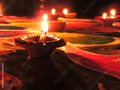 low angle shot of diwali oil clay lamps with intricate design burning with a glowing flame placed on multicoloured rangoli background