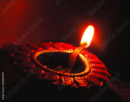Close up isolated low key diwali oil clay lamp, chirag or panti shot with a dutch angle diagonal framing on a dark orange black background