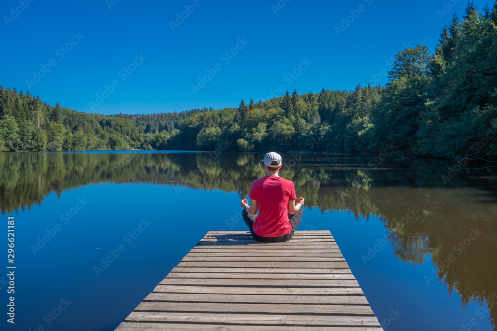 Beulotte Saint Laurent, France - 09 12 2019: Hike in the circuit of the thousand ponds. a girl sitting on a wooden pontoon, doing yoga in front of the pond