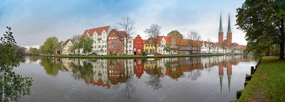 Cityscape, old town of Luebeck in Germany, wide panoramic view from Malerwinkel, meaning painter's corner, to the historic city at the river Trave with reflections, copy space in the cloudy blue sky