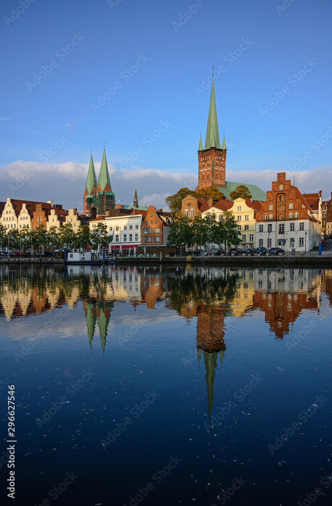 Cityscape of the historic old town of Luebeck in Germany with reflection in the river Trave, illuminated by the setting sun late afternoon, dark blue water and sky, copy space