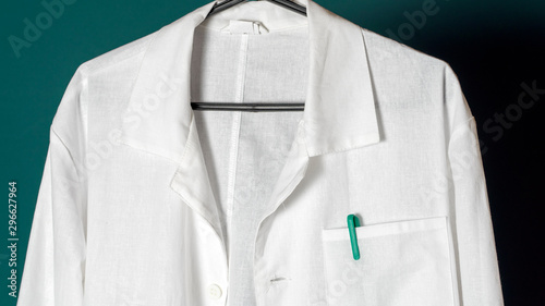Closeup of a doctor's white lab coat on a hanger against a dark background.