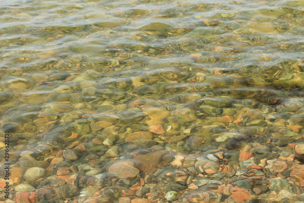 Multi-colored stones under water with light waves and highlights. Top view at a slight angle. Texture for creative design.