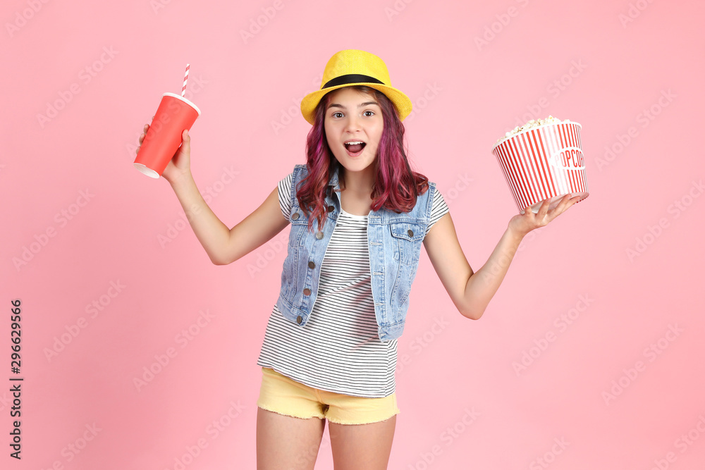 Young girl holding bucket with popcorn and paper cup on pink background Young girl holding bucket with popcorn and paper cup on pink background