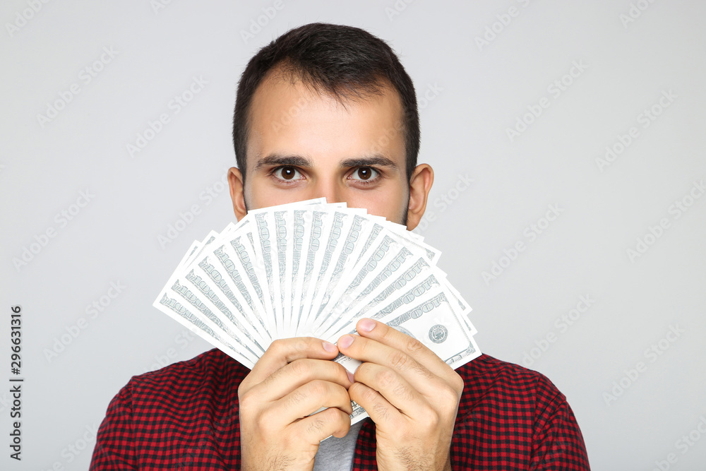 Young happy man holding dollar banknotes on grey background Young happy man holding dollar banknotes on grey background