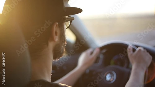 Close-up of young bearded man driving car, with sunlight effect of sunset.