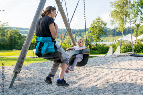 Mother and daughter swinging in a playground at local park.