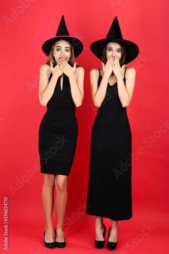 Two young women in black halloween costumes on red background