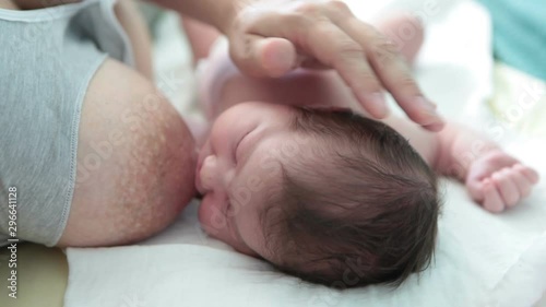 Newborn baby lying back near mother breast, breastfeeding. Close up view at Caucasian baby and female hand covering infant head photo