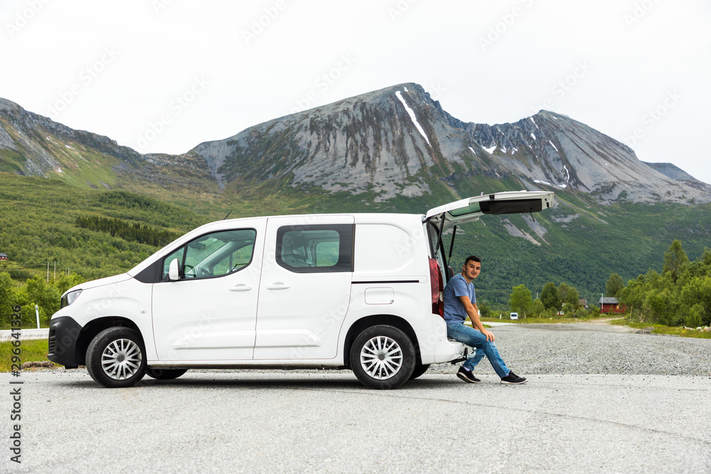 Young man sits in the car trunk on mountains view