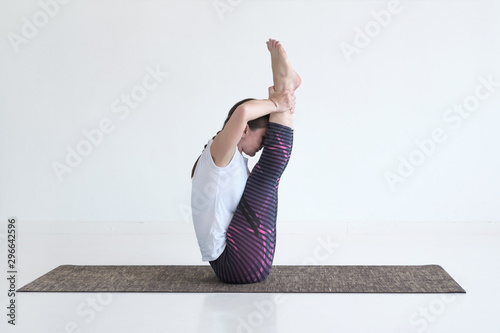 Sporty caucasian woman doing exercises for legs and abs, sitting in Ubhaya Padangusthasana asana, Both Big Toe pose, studio full length photo
