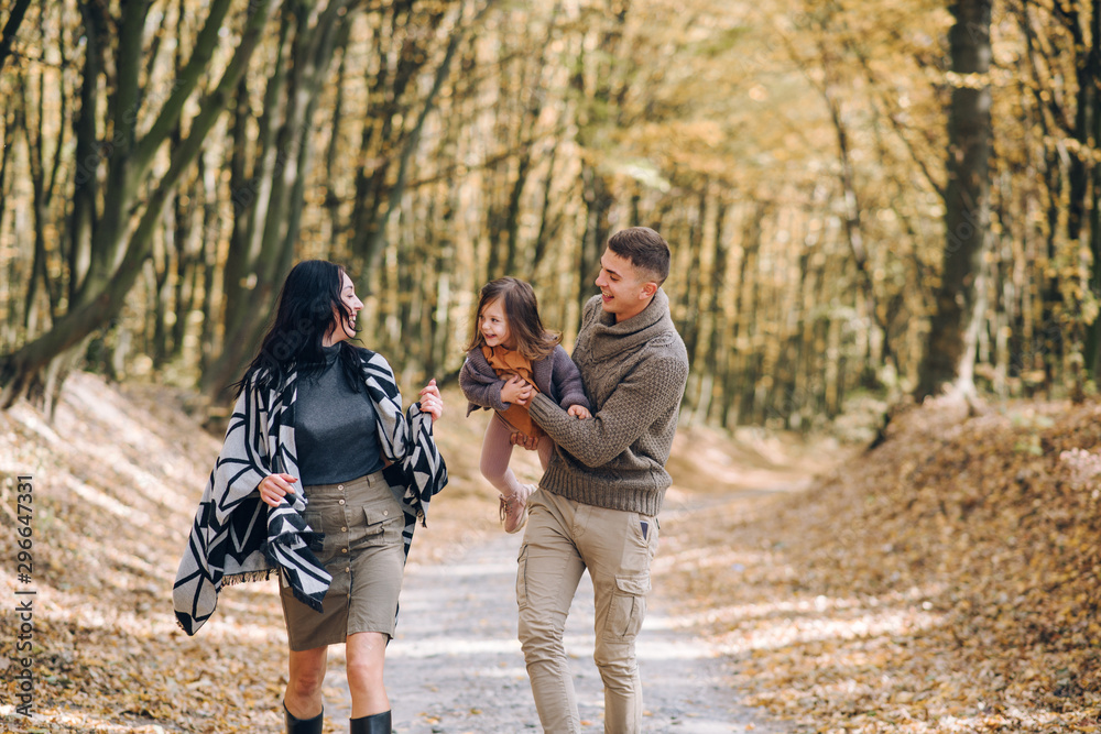 Beautiful young family walking in the autumn forest. Family walking in an autumn park with fallen fall leaves. Warm autumn