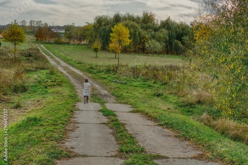 Obraz na płótnie a lonely woman specifying a dirt road in the autumn landscape of fields, trees and bushes w salonie
