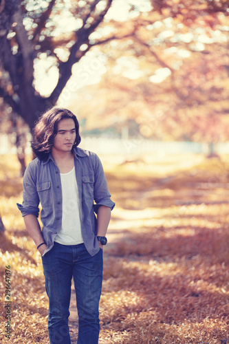 Asian long hair man Walking in the garden The background is a tree and the sunlight in autumn. © Other Edge