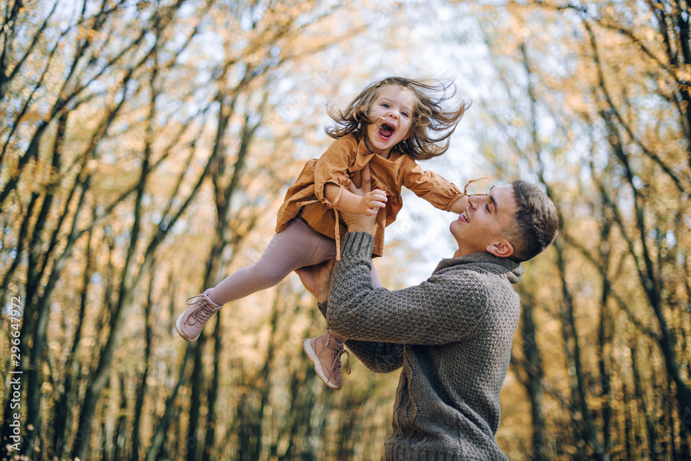 Obraz premium Family autumn weekend. Young father and his little daughter together in autumn park outdoors. Beautiful baby with leaves on top of dad.