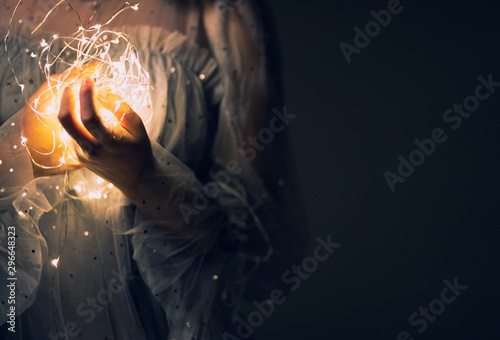 Hands are holding sparkling lights or fairy light on a white with a dim yellow light on dark background.