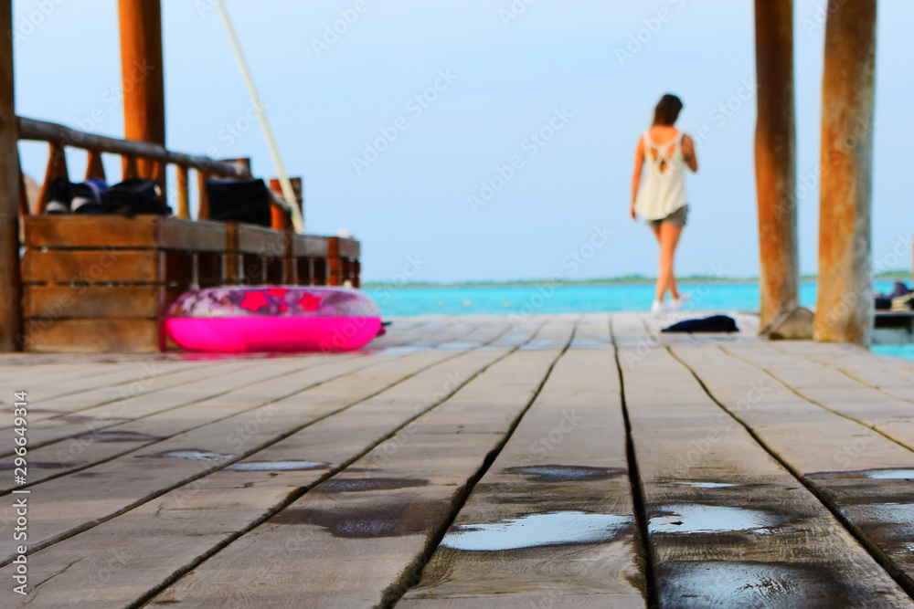 Young girl on vacation. Wooden floor on sea water. Pink lifesaver. Wet floor. Unfocused person