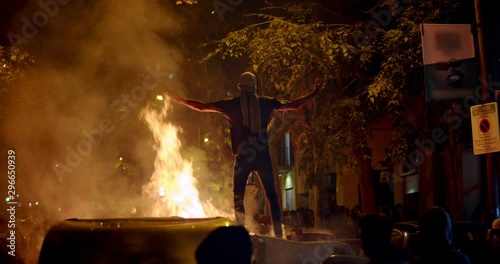 Young rebel riot revolutionary anarchist stands on trash and fire showing fuck as protest for independence on demonstration about the proces and political prisoners Demonstrator burns garbage bins in photo