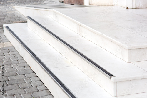 entrance with a marble threshold with stone steps and a white ramp to the exterior on the streets with a pavement of gray tiles. photo