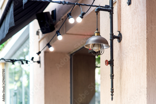 street lamp in loft style on the wall of the facade of the building with a garland of light bulbs and a canopy over the window.
