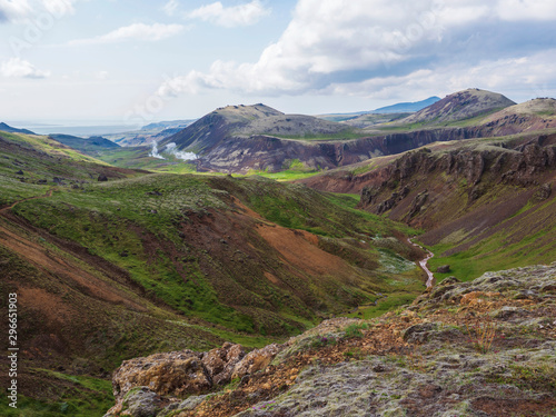 Reykjadalur valley with hot springs river with lush green grass meadow and hills with geothermal steam. South Iceland near Hveragerdi city. Summer sunny morning, blue sky. photo