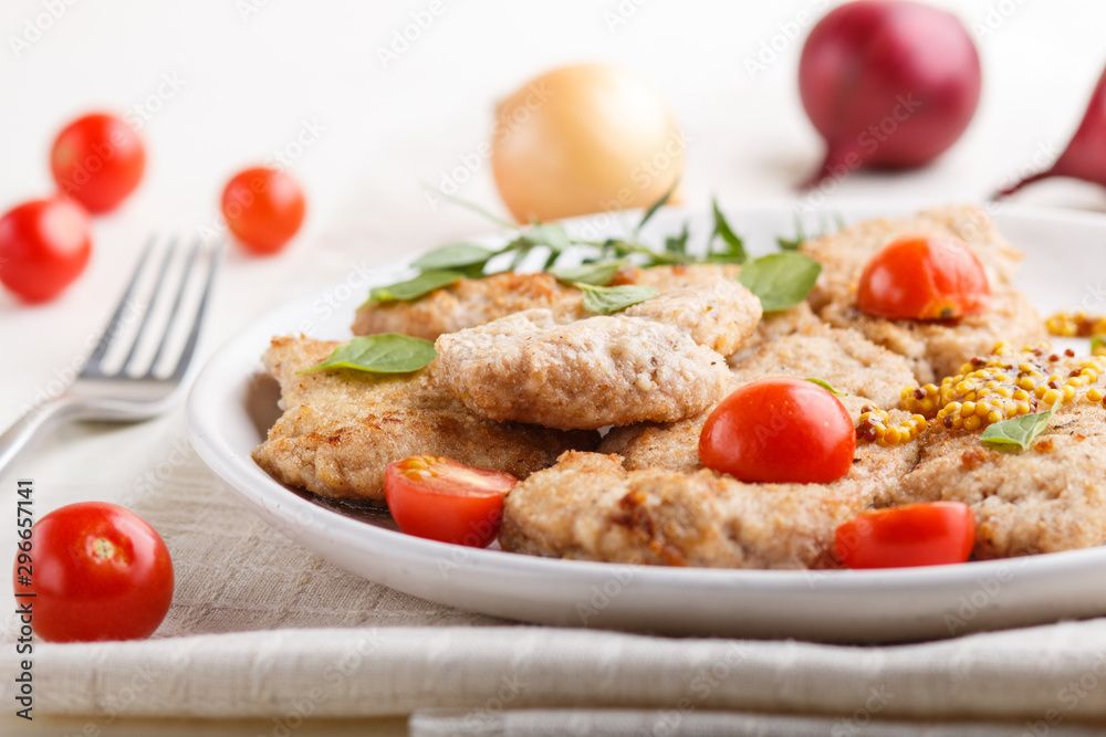 Fried pork chops with tomatoes and herbs on a white ceramic plate on a white wooden background. side view, close up. Fried pork chops with tomatoes and herbs on a white ceramic plate on a white wooden background. side view, close up.