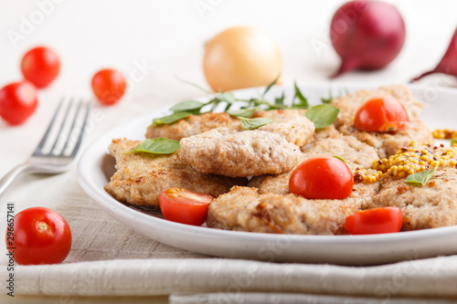 Fried pork chops with tomatoes and herbs on a white ceramic plate on a white wooden background. side view, close up.