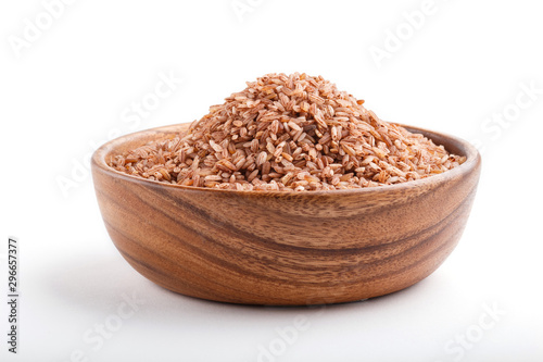 Wooden bowl with unpolished brown rice isolated on white background. Side view.