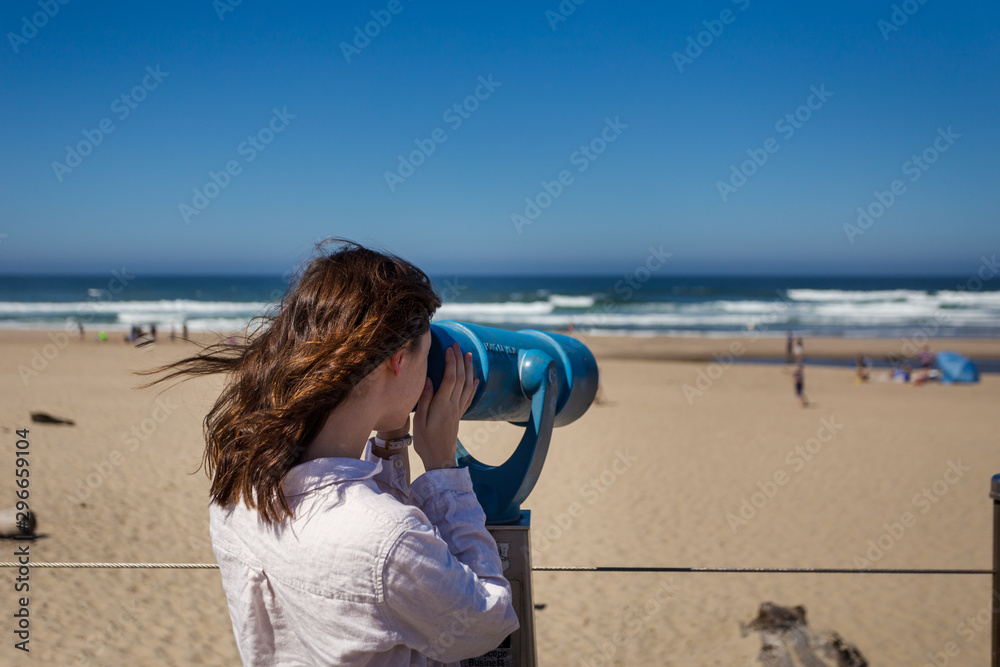 Shot of an attractive young woman looking through a viewing telescope at the beach of the Oregon coast near Lincoln City.
