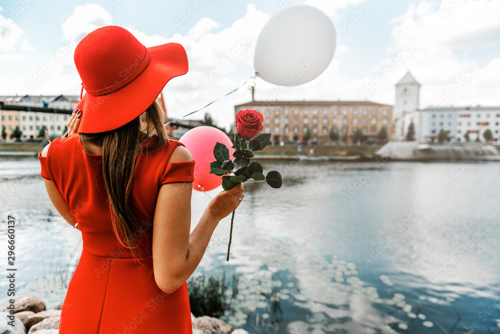 Girl in red hat and dress from behind with a rose.
