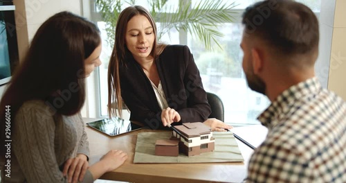 Real estate manager showing architectural model of house to clients in real estate sales department, concluding deal