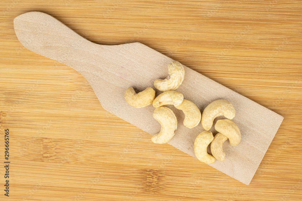Group of nine whole brown nut cashew on wooden cutting board flatlay on light wood Group of nine whole brown nut cashew on wooden cutting board flatlay on light wood