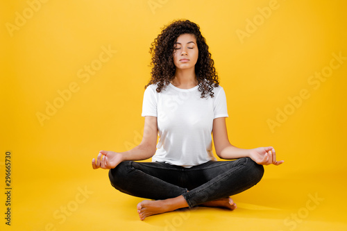 relaxed black woman meditating in yoga pose isolated over yellow