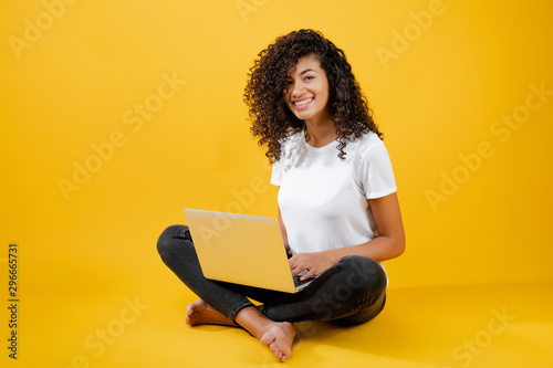 happy african black woman sitting with laptop isolated over yellow
