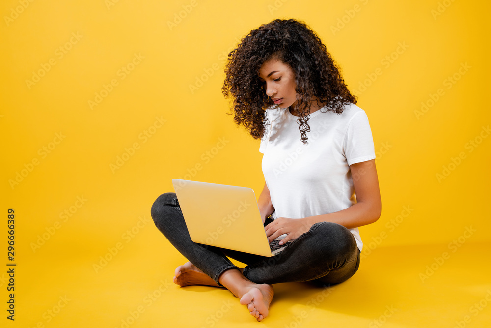 Naklejka premium happy african black woman sitting with laptop isolated over yellow