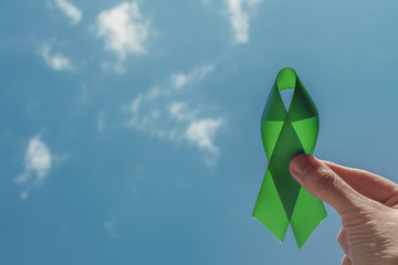 hand holding Green Ribbon over blue sky, Mental health awareness and Lymphoma Awareness, World Mental Health Day