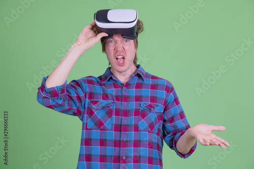 Confused young hipster man removing virtual reality headset and shrugging shoulders