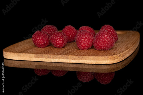 Lot of whole fresh red raspberry on bamboo cutting board isolated on black glass photo