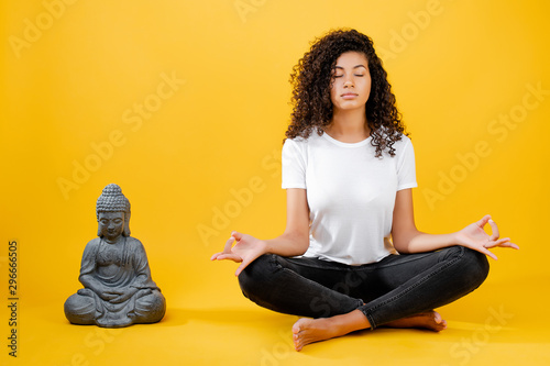 calm young black woman meditating and doing yoga with buddha isolated over yellow