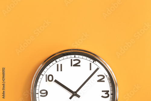 Part of analogue plain wall clock on trendy pastel orange background. Ten o'clock. Close up with copy space, time management or school concept and summer or winter time change photo