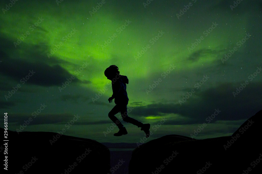Sillhouette of preschool child, jumping over gap on aurora borealis sky background