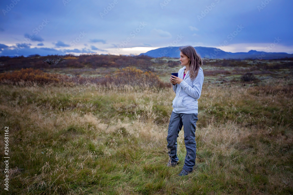 Fototapeta premium Young woman, drinking coffee or tea, early in the morning in camping, enjoying the beautiful autumn view