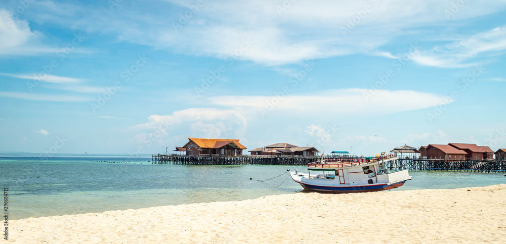 Beautiful view of crystal clear water, white sand, blue sky, traditional cottage, and wooden boat at Derawan Island, Indonesia