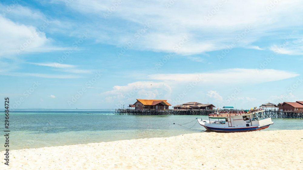 Obraz premium Beautiful view of crystal clear water, white sand, blue sky, traditional cottage, and wooden boat at Derawan Island, Indonesia