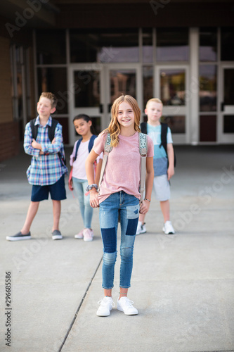 Group of Elementary school students standing in front of their school. Smiling and hanging out together after school. Selective focus on the cute girl in front