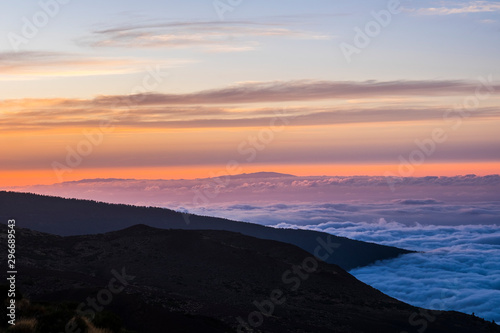 Sunset or sunrise beautiful landscape moment at the mountain - high peak vulcan and coloured sunlight in background - blue sea of clouds - beauty of outdoor nature